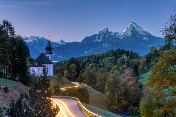 Mount Watzmann and the small Maria Gern church at dawn with light traces from a car headlight