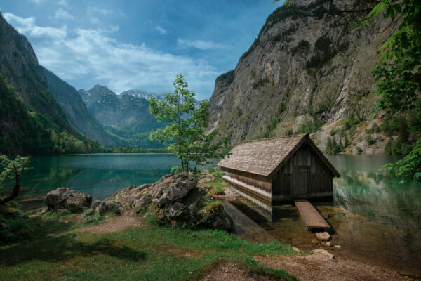 Boathouse with mountain cliffs on lake Obersee at Berchtesgaden Bavaria, clouds in blue sky, turquoise calm water, Berchtesgaden Bavaria